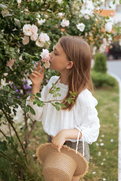 Belle petite fille avec un chapeau de paille près d'un buisson de roses blanches