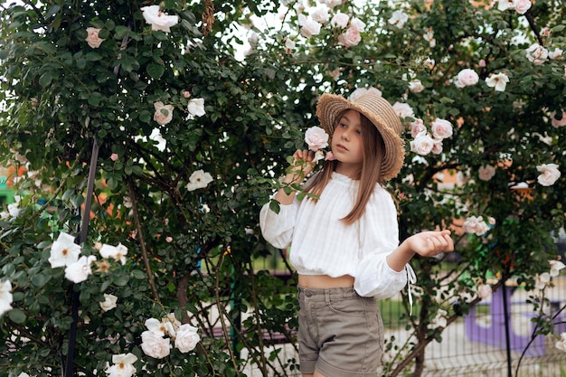 Belle petite fille avec un chapeau de paille près d'un buisson de roses blanches