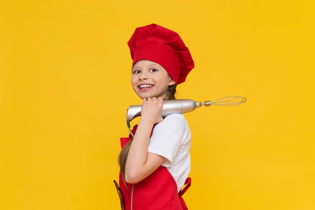 Belle petite fille chef dans un costume de cuisine et tenant un batteur électrique Petite fille chef sur un fond isolé