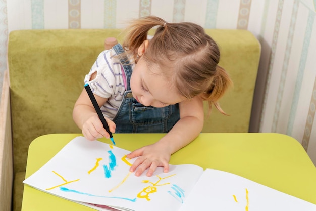 belle petite fille concentrée sur le dessin avec un marqueur dans un carnet de croquis