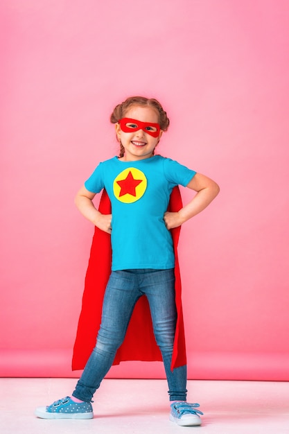 Belle petite fille en costume de super-héros en cape rouge et masque montre à quel point