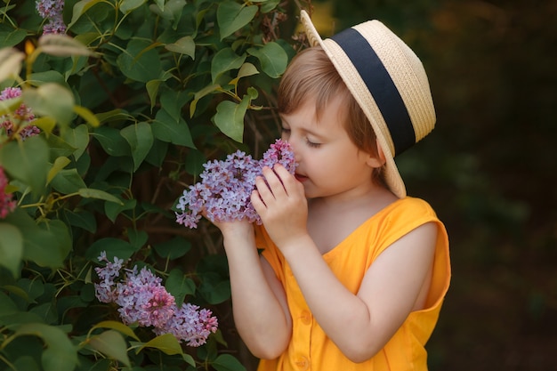 Belle petite fille dans un chapeau près de fleurs lilas