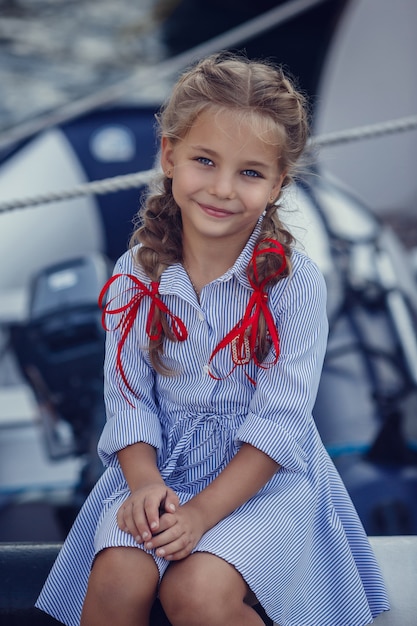 Une belle petite fille dans un style marin sur fond de bateaux et de yachts.