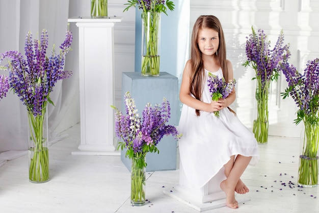 Belle petite fille émotionnelle est assise parmi les fleurs violettes. Un décor fleuri dans un intérieur