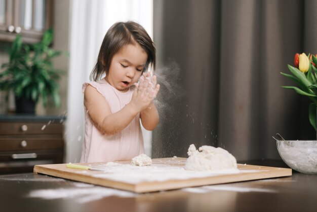 Belle petite fille frappe des mains avec de la farine enfant joue avec de la farine dans la cuisine