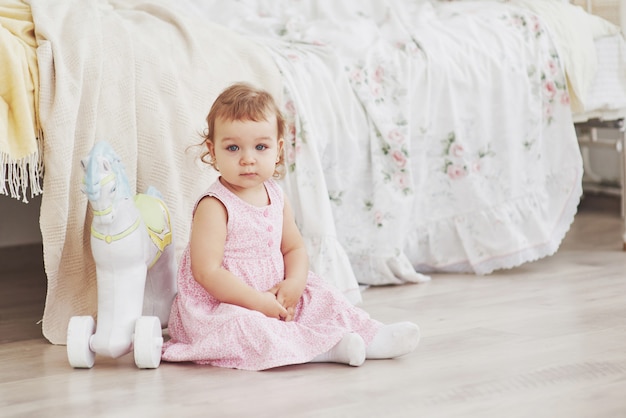 Belle petite fille jouant des jouets. Blonde aux yeux bleus. Chaise blanche. La Chambre des enfants. Portrait de petite fille heureuse. Concept d'enfance