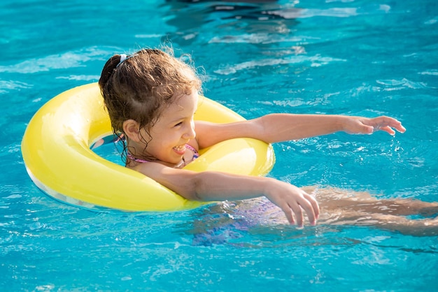 Une belle petite fille en maillot de bain et dans un cercle gonflable jaune se baigne et joue dans la piscine