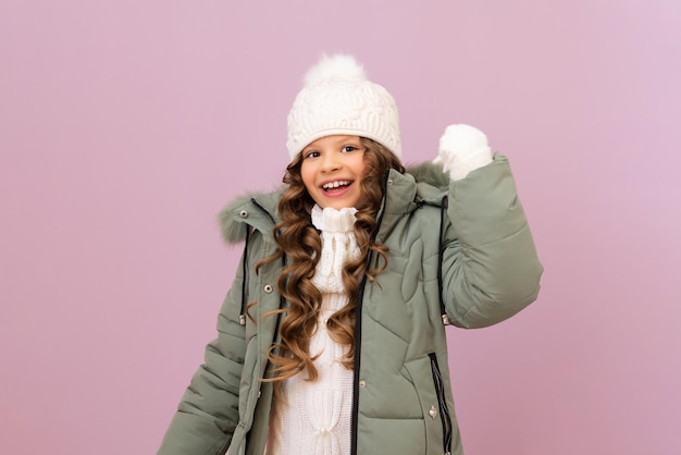 Une belle petite fille montre de la joie que l'hiver est arrivé. L'enfant est très heureux avec de bons vêtements d'hiver chauds et de bonne qualité. Bébé dans une veste chaude et un bonnet tricoté.