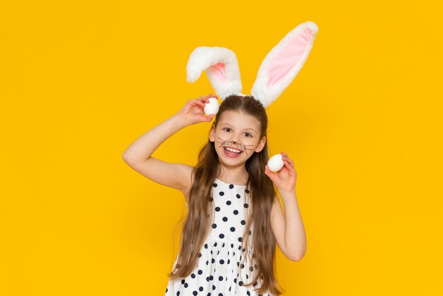 Une belle petite fille avec des oreilles de lapin en fourrure sur la tête tient des œufs de poule dans ses mains pour les peindre pour les vacances de Pâques