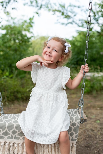 Belle petite fille passe du temps à l'extérieur à cheval sur une balançoire en souriant et en grimaçant