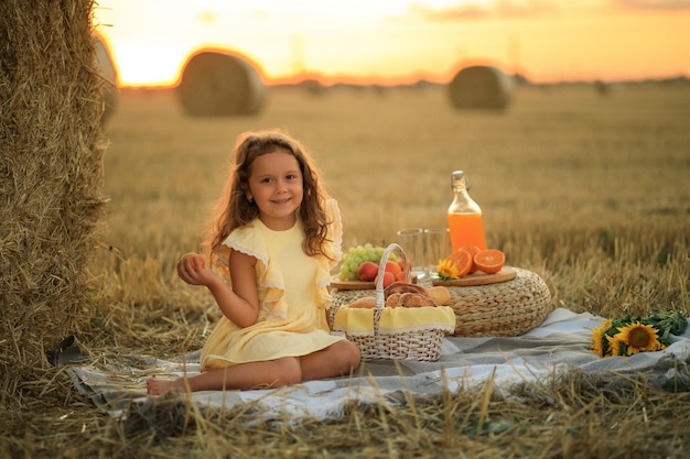 Belle petite fille sur un pique-nique dans un champ près d'une pile de portrait de foin sec dans un coucher de soleil ensoleillé