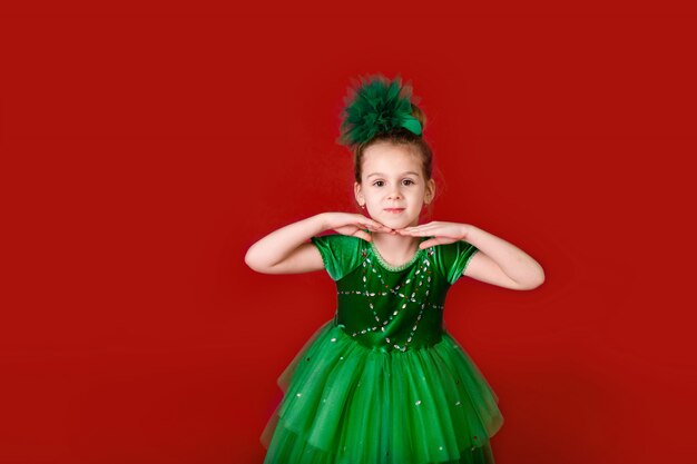 Belle petite fille princesse dansant en robe verte de luxe isolée sur mur rouge. Fête de carnaval avec costumes