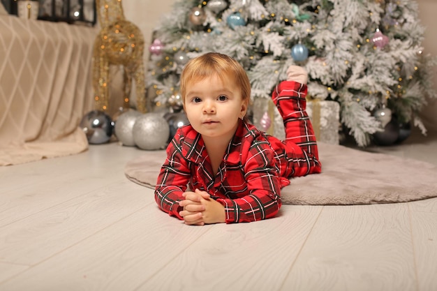 une belle petite fille en pyjama de Noël rouge dans une cage se trouve à l'arbre de Noël