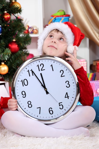Belle petite fille avec réveil en prévision du Nouvel An dans une salle décorée de façon festive