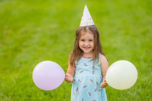 Belle petite fille en robe bleue et chapeau avec des ballons dans le parc joyeux anniversaire
