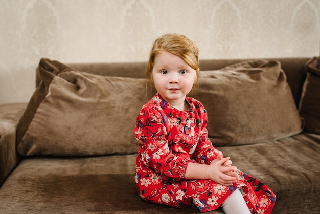 Belle petite fille en robe est assise sur le canapé à la maison