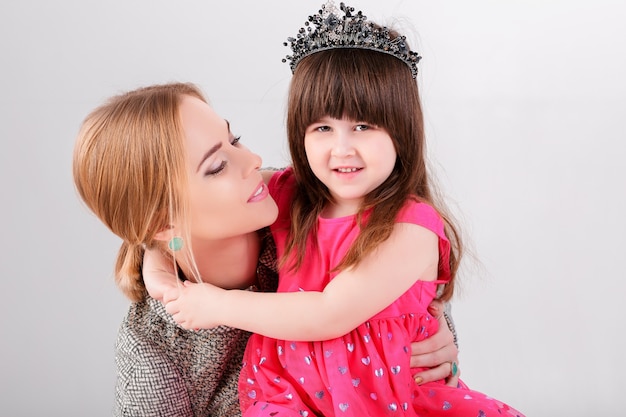 Belle petite fille en robe de princesse rose avec une couronne et belle mère étreignant sur un fond gris.