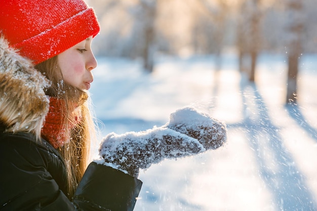 Belle petite fille soufflant des flocons de neige dans la forêt blanche d'hiver couverte de neige