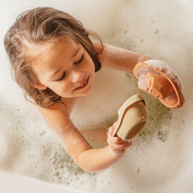 Belle petite fille souriante assise dans un bain moussant et jouant avec de jolis petits bateaux jouets en silicone beige et orange Jouets pour bébé jouets pour développer la créativité concept de jeux d'eau utilisation Instagram