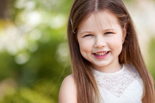 Belle petite fille souriante en robe crème, contre le vert du parc d'été