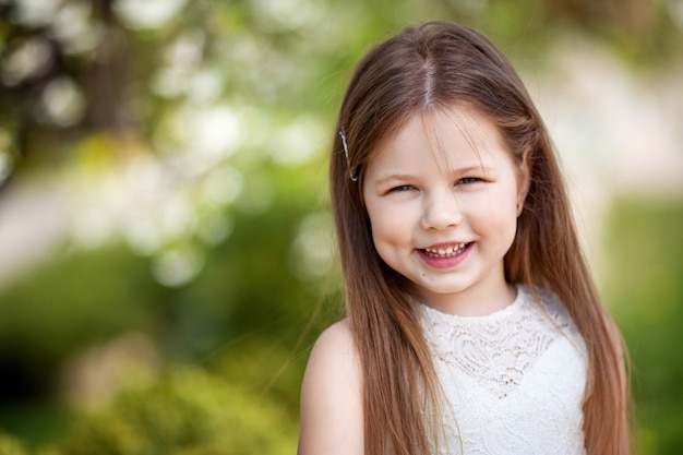 Belle petite fille souriante en robe crème, contre le vert du parc d'été