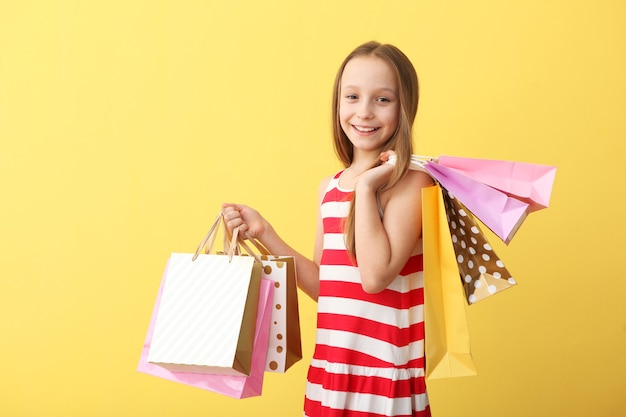 Belle petite fille souriante avec des sacs pour faire du shopping sur un fond coloré