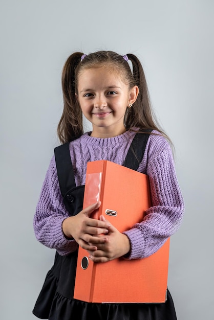 Belle petite fille souriante tenant des livres épais dans ses mains isolées sur fond uni