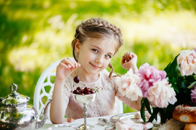 Belle petite fille tenant des cerises à la main sur un bel ensemble de table élégant