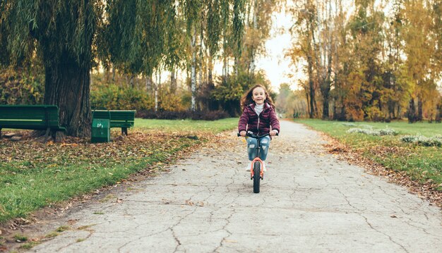 Belle petite fille à vélo marchant dans le parc seul dans une journée d'automne