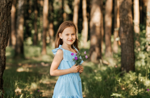 Belle petite fille vêtue d'une robe bleue avec des fleurs dans la nature en été