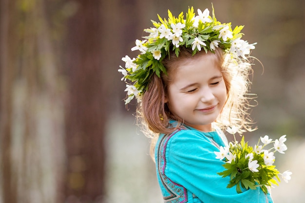 Belle petite fille vêtue d'une robe bleue marchant dans le bois de printemps. Portrait de la jolie fille avec une couronne de fleurs sur la tête. Enfant jouant à l'extérieur en été. Temps de Pâques. Espace copie