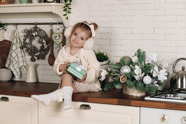 Belle petite fille vêtue d'une robe avec un cadeau à la main, assis sur la table de la cuisine