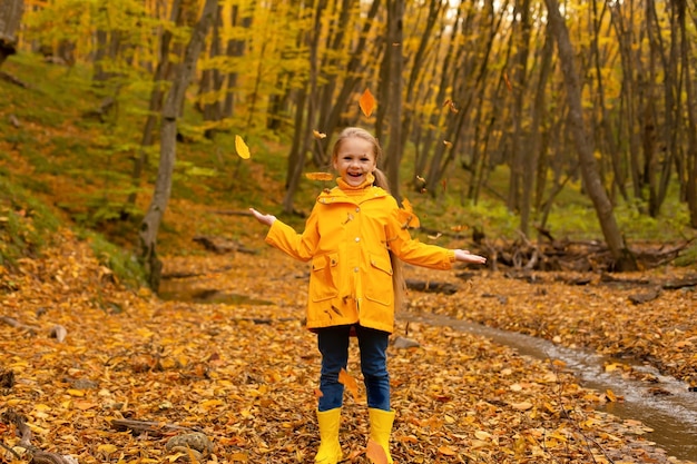 une belle petite fille vêtue d'une veste jaune et de bottes se promène dans la forêt d'automne urbaine