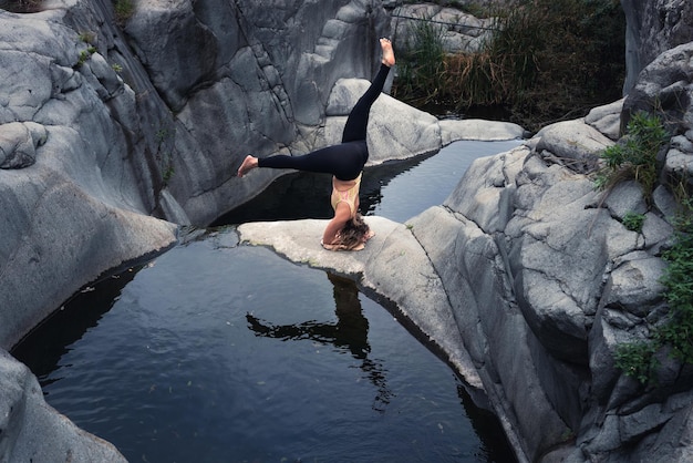 Belle photo d'une jeune femme intrépide faisant du yoga près d'une haute rivière de montagne rocheuse