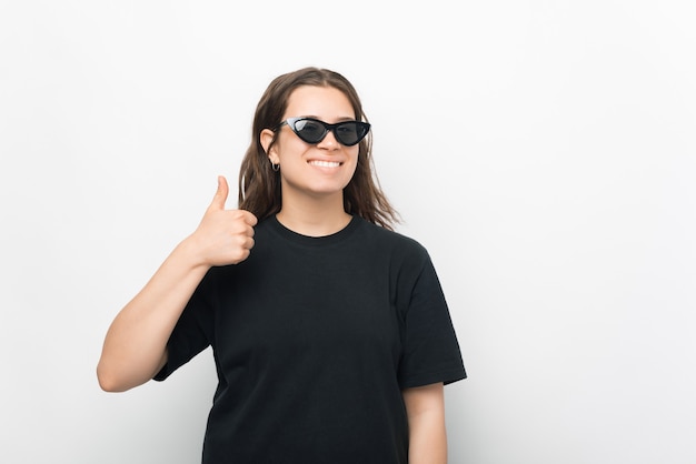 Une belle photo d'une jeune femme souriante à la caméra avec des lunettes de soleil montre un pouce vers le haut