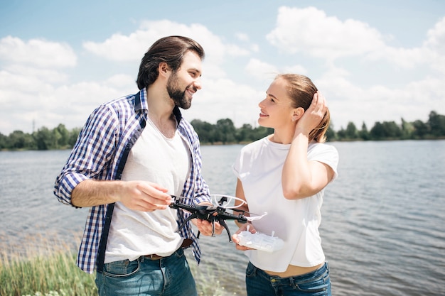 Belle photo de jeune homme et femme debout ensemble et se regardant. Ils sont amoureux l'un de l'autre. Guy tient un drone dans les mains. La femme tient ses mains sur les cheveux.