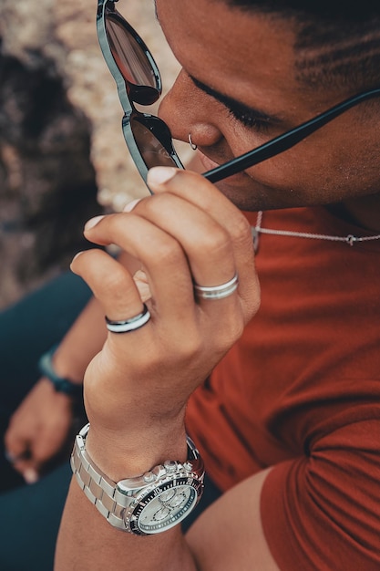 Une belle photo d'un jeune homme en train d'enlever ses lunettes de soleil alors qu'il est assis sur les rochers près du lac