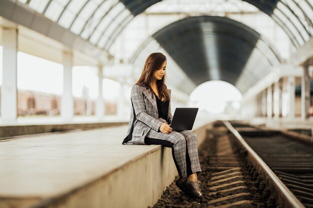 Belle pigiste féminine utilisant un ordinateur portable pour le travail à distance en attendant le train.