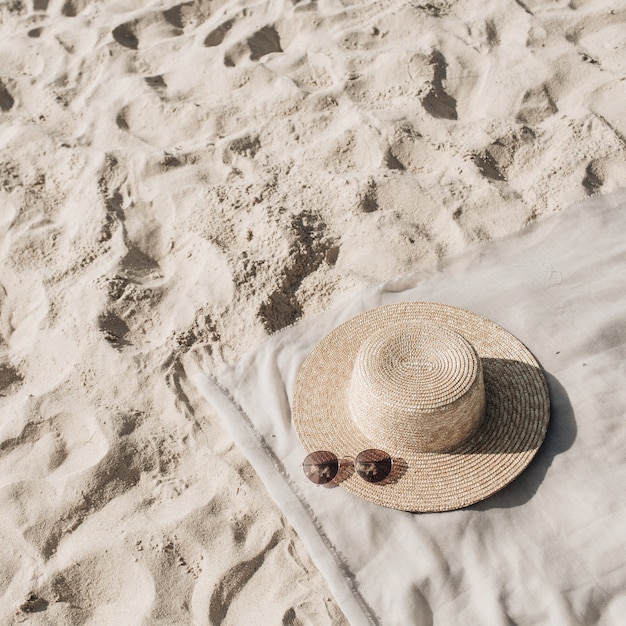 Belle plage tropicale avec du sable blanc, des marches de pied, une couverture neutre avec un chapeau de paille et des lunettes de soleil