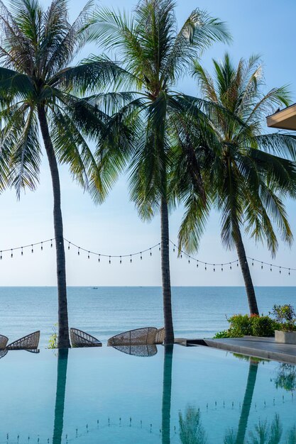 Belle plage tropicale et mer avec palmier cocotier et chaise autour de la piscine de l'hôtel pour les voyages et les vacances reposantes l'été dans la piscine à débordement en regardant la vue