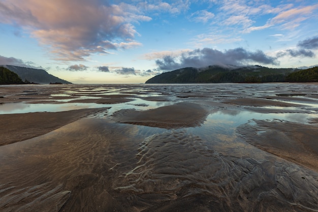 Belle plage vide avec des nuages dramatiques et des ondulations de la marée dans le sable.