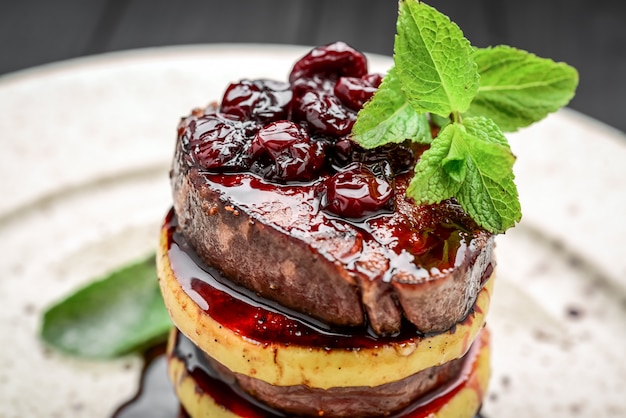 Une belle présentation de viande frite avec une pomme, romarin, sauce aux cerises