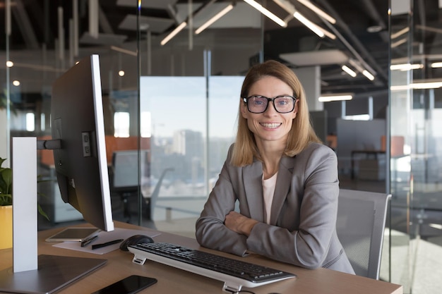 Belle et réussie femme d'affaires à lunettes regarde la caméra et sourit comptable travaillant dans un bureau moderne