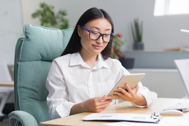 Une belle et réussie femme d'affaires travaille dans un bureau moderne une femme asiatique utilise une tablette comp