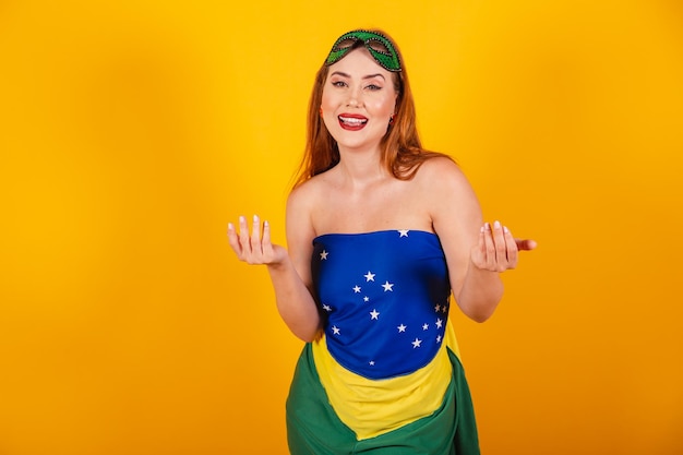 Belle rousse brésilienne avec des vêtements de carnaval faits avec le drapeau brésilien invitant avec les mains