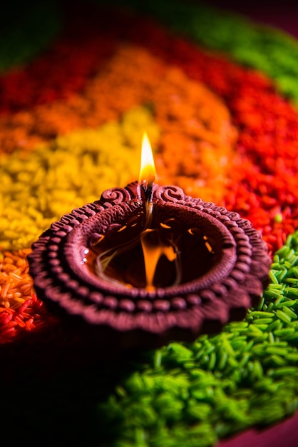 Belle salutation Diwali à l'aide de Diya ou d'une lampe à huile en argile allumée et disposée sur Rangoli faite de grains de riz multicolores, mise au point sélective