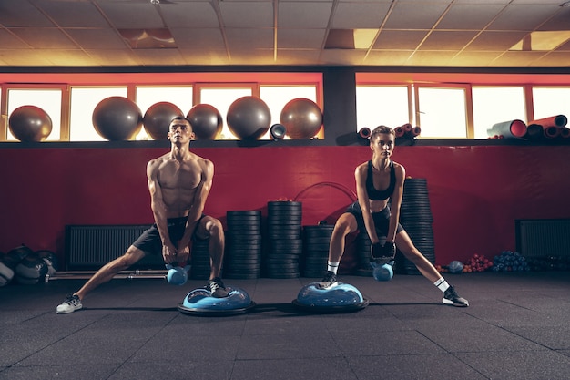 Belle séance d'entraînement de jeune couple sportif dans la salle de gym ensemble. Homme de race blanche s'entraînant avec une formatrice. Concept de sport, d'activité, de mode de vie sain, de force et de puissance. Travailler avec des poids.