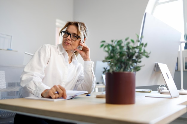 Belle secrétaire adulte dans une chemise blanche et des lunettes est assise sur le lieu de travail