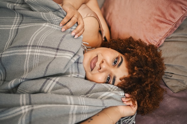 Belle sinueuse grande taille femme noire afro cheveux afro allongé sur le lit avec une couverture à carreaux grise confortable