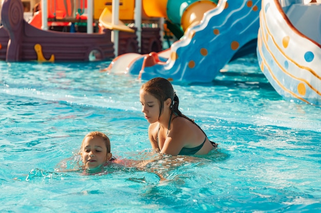 Une belle sœur aînée aide sa petite sœur cadette à apprendre à nager dans une piscine à l'eau claire et transparente